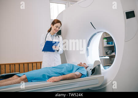 Schöne Radiologe holding Zwischenablage während der Vorbereitung des Patienten für die Tomographie Stockfoto