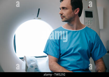 Nachdenklich sitzenden Patienten auf CT-Scanner Bett im Krankenhaus und weg schauen Stockfoto