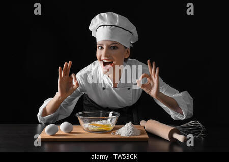 Junge weibliche Küchenchef auf dunklem Hintergrund Stockfoto