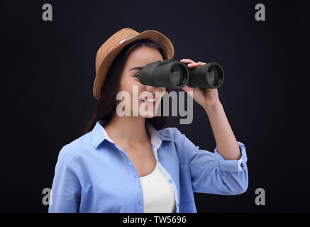 Schöne junge Frau mit Fernglas auf dunklem Hintergrund Stockfoto