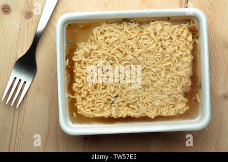 Pflegende Nudeln auf einem hölzernen Tisch in einer Wegwerf- Platte. Stockfoto