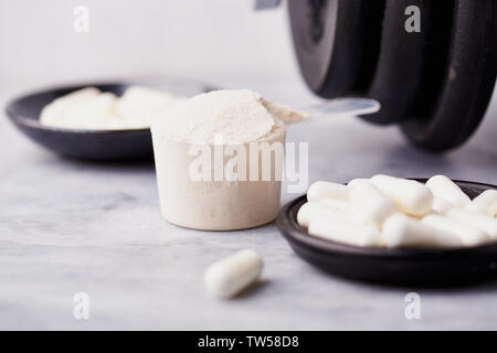 Messlöffel Whey Protein, Creatin, Taurin Kapseln und eine Hantel. Bodybuilding Nahrungsergänzungen auf Stein/Holz- Hintergrund. Close Up. Kopieren Sie Platz. Stockfoto