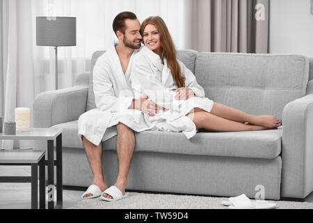 Junge liebende Paar in Bademänteln auf dem Sofa zu Hause sitzen Stockfoto