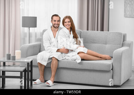 Junge liebende Paar in Bademänteln auf dem Sofa zu Hause sitzen Stockfoto