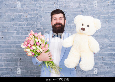 Macho fertig, romantisches Date. Warten auf Darling. Mann gut gepflegt Verschleiß tuxedo Bow Tie halten Blumen Tulpen Bouquet und großen Teddybären Spielzeug. Laden Sie dating. Romantisches Geschenk. Romantischen Mann. Stockfoto