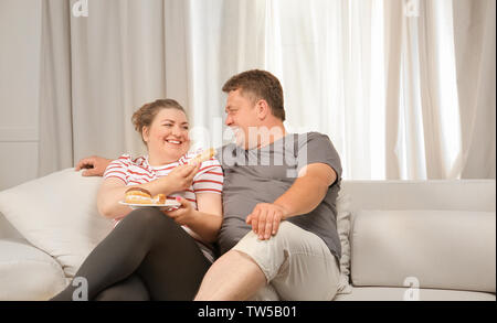 Übergewicht paar Süßigkeiten essen auf dem Sofa zu Hause Stockfoto