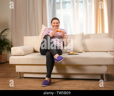 Übergewichtige junge Frau Süßigkeiten essen auf dem Sofa zu Hause Stockfoto