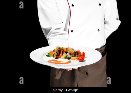 Koch Holding frisch zubereitetes Gericht auf schwarzen Hintergrund, Nahaufnahme Stockfoto