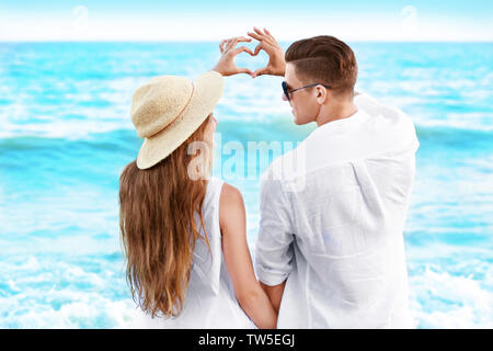 Glückliches junges Paar Herzen bilden mit ihren Fingern auf das Meer Strand Stockfoto