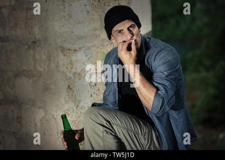 Mann sitzend mit Zigarette und einer Flasche Alkohol in verlassenen Gebäude Stockfoto