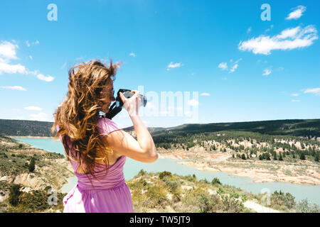 Langhaarigen weiblichen Touristen in ein rosa Kleid mit einer Kamera steht in den Bergen Stockfoto