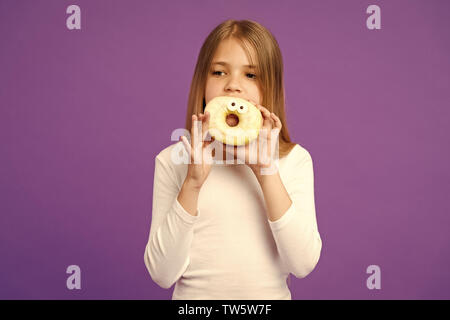 Mädchen, dass große Krapfen mit Puderzucker. Süßes, verglaste Bagel mit Augen. Kind essen lustig Dessert, süße Kindheit. Kind mit langen Haaren tragen weiße Outfit auf Violett Hintergrund isoliert. Stockfoto