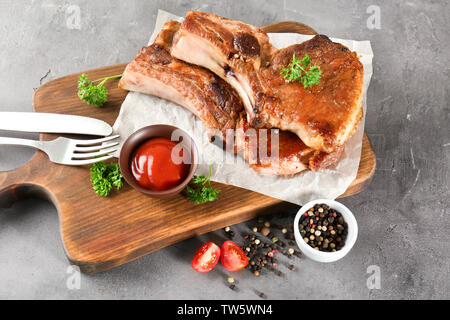 Holzbrett mit köstlichen gegrillten Rippchen und Tomatensauce auf Tisch Stockfoto