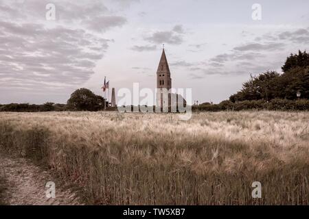 Kirche und Denkmal in der berühmten französischen Dorf Colleville-sur-Mer im Abstand von einem Weizenfeld gesehen bei Sonnenuntergang - französische Landschaft Stockfoto