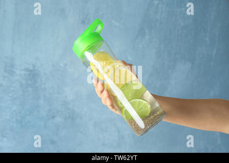 Hand, die eine Flasche Wasser mit Chia Samen und Zitrone auf hellen Hintergrund Stockfoto