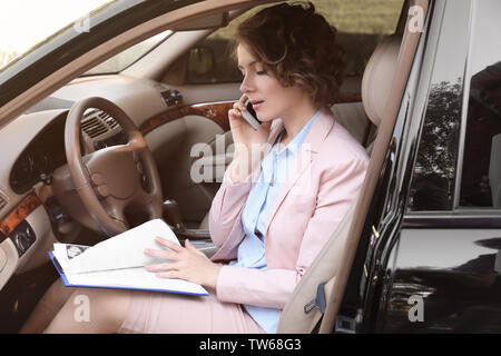 Junge Geschäftsfrau mit Papieren am Telefon sprechen im Auto. Stockfoto