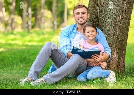 Junger Mann und seine kleine Tochter lesen Buchen Sie im Park Stockfoto
