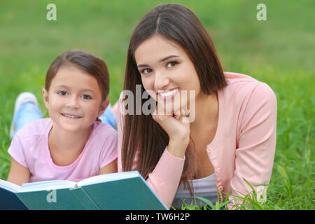 Junge Frau und ihre kleine Tochter lesen Buchen Sie im Park Stockfoto