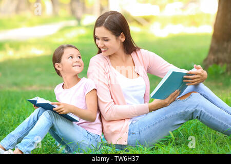 Junge Frau und ihre kleine Tochter Bücher lesen im Park Stockfoto