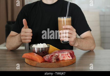 Mann hält Glas mit Protein Shake am Tisch Stockfoto
