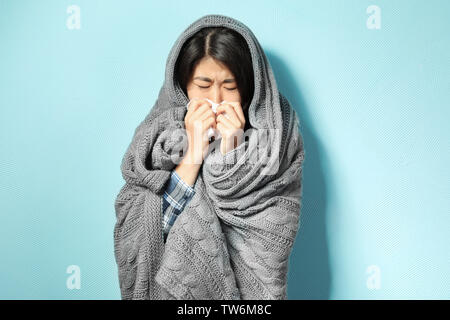 Kranke junge Frau in Decke auf Farbe Hintergrund gewickelt Stockfoto