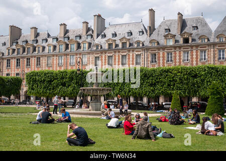 Paris, Frankreich, 25. Mai 2019: Place des Vosges. Menschen entspannend auf den grünen Rasen der berühmten Place des Vosges - älteste geplante Platz im Viertel Marais. Stockfoto