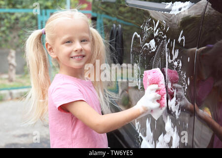 Adorable kleine Mädchen waschen Auto mit Schwamm im Freien Stockfoto