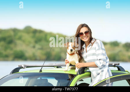 Schöne junge Frau mit niedlichen Hund in der Nähe von Auto auf dem Fluss Ufer Stockfoto