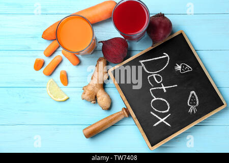Kleine Schiefertafel mit Wort DETOX, frische Säfte in Gläsern und Zutaten auf Tisch Stockfoto