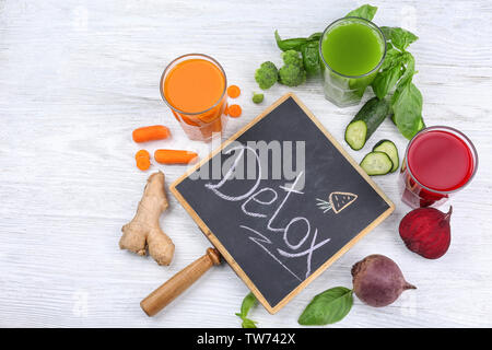 Kleine Schiefertafel mit Wort DETOX, frische Säfte in Gläsern und Zutaten auf Tisch Stockfoto