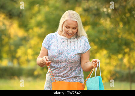 Gerne reife Frau mit Einkaufstüten im Freien Stockfoto
