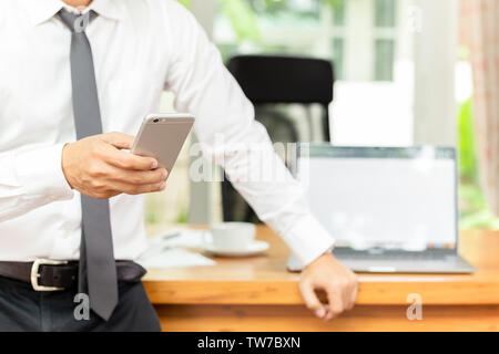 Businessmans hand Handy mit Laptop auf dem Schreibtisch aus Holz. Stockfoto