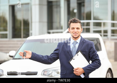 Verkäufer mit Schlüssel in der Nähe von neuen Autos im Freien Stockfoto