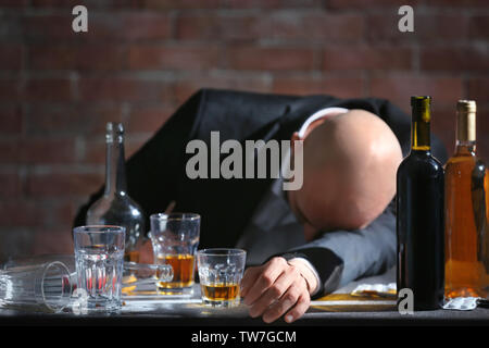 Betrunkener mann am Tisch mit Flaschen Alkohol und Gläser. Alkoholismus Konzept Stockfoto