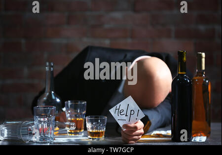 Betrunkener mann am Tisch sitzen und halten Papier mit Wort helfen. Alkoholismus Konzept Stockfoto