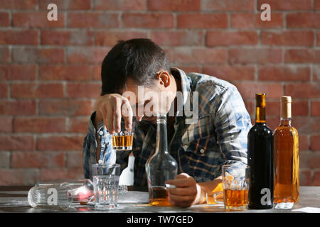 Betrunkener mann am Tisch mit Alkohol und Drogen zu sitzen. Alkoholismus Konzept Stockfoto