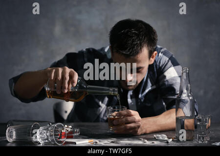 Mann am Tisch sitzen und gießt Whiskey in Glas. Alkoholismus Konzept Stockfoto