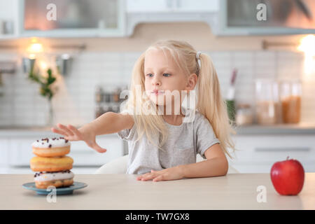 Kleine süße Mädchen die Wahl zwischen süßen Krapfen und frischen Apfel in der Küche Stockfoto