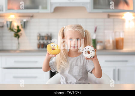 Kleines Mädchen mit süßen Krapfen am Küchentisch Stockfoto