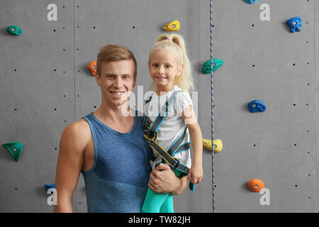 Kursleiter Holding kleines Mädchen in Kletterhalle Stockfoto