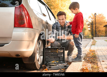 Junger Vater mit niedlichen jungen Reifen wechseln, im Freien Stockfoto