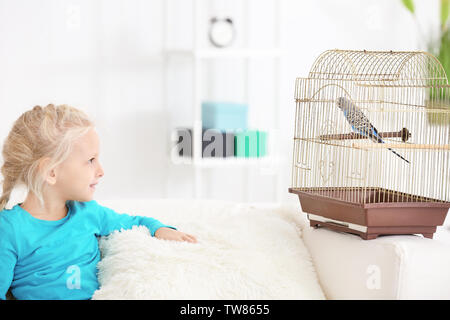 Kleines Mädchen mit niedlichen pet Blue Parrot im Käfig auf dem Sofa im Innenbereich Stockfoto