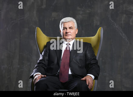 Stattliche reifer Mann im Sessel sitzt auf dunklem Hintergrund Stockfoto