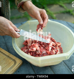 Frau Schneiden von rohem Fleisch mit einem Messer auf einen Tisch, Outdoor close-up Stockfoto