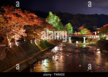 Nächtliche Herbst Landschaft der Martk von Fluss in der Stadt Takayama mit beleuchteten Bunte rote und grüne Bäume entlang der Ufer und roten Nakahashi Brücke Stockfoto