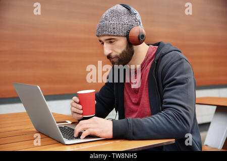 Junge hipster Mann mit Laptop Musik im Café im Freien Stockfoto