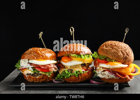 Mit leckeren Burger auf Tabelle auf schwarzem Hintergrund Platte Stockfoto