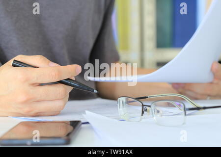 Mann Schreiben auf Papier auf dem Tisch in einem Büroraum. mobile Gerät in der Nähe abgelegt Neben. Schreibarbeit tun auf weißer Tisch. Brillen auf dem Schreibtisch Platz in Stockfoto