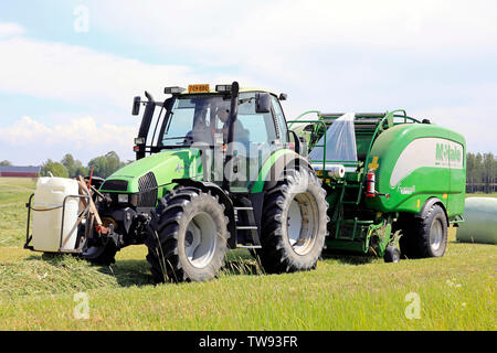 Salo, Finnland. Juni 15, 2019. Bauer arbeiten mit Deutz-Fahr Agrotron Traktor und McHale 3 plus integrierte Ballenpresse im Heu Feld am Tag des Sommers Stockfoto