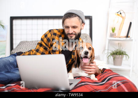 Hübscher junger Hipster mit seinem Hund ruht auf Bett zu Hause Stockfoto